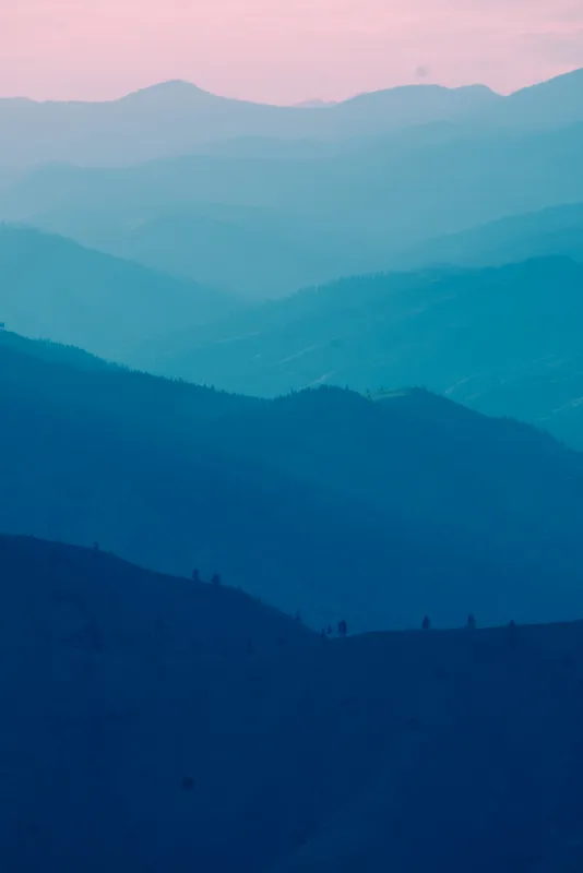 Layered blue mountain ridges fading up into a pink sky
