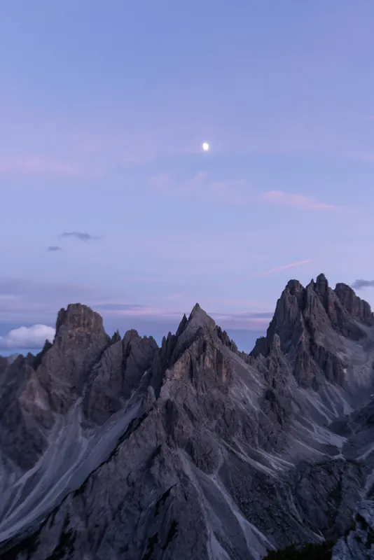 Jagged mountain peaks at dusk under a lavender sky, the moon above